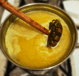 a pot of cooked mushurir dal with a dal ghotni (masher)